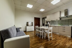Una cocina moderna con armarios blancos, una mesa de comedor con sillas, un televisor de pantalla plana y suelo de madera.