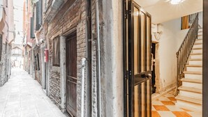 A narrow alleyway with a brick building, a wooden door, and a staircase with a checkered floor. - GuestHost - The Venice Red Door Aparment (Venezia)