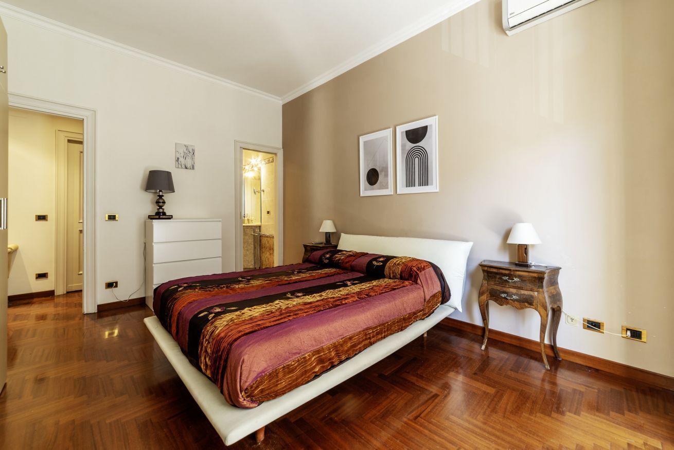 Une chambre à coucher avec un grand lit, des tables de chevet, une armoire et une porte donnant sur une autre pièce.
