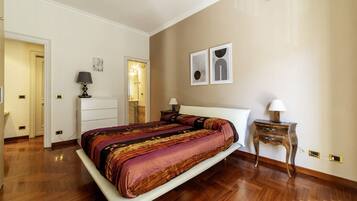 Une chambre à coucher avec un grand lit, des tables de chevet, une armoire et une porte donnant sur une autre pièce.