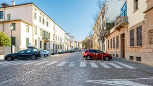Una calle empedrada flanqueada por edificios históricos, un paso de peatones y coches estacionados.