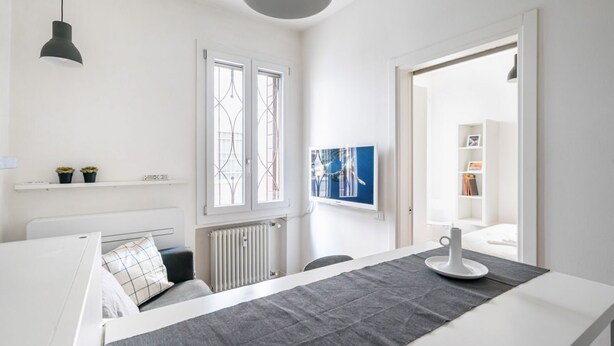 Una habitación moderna y minimalista con cama, mesita de noche y ventana con reja decorativa.