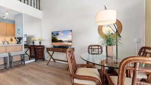 A dining area with a glass table, wicker chairs, a television, and a potted plant. - Convenient to downtown Kihei, across famous Charley Young Beach, 3 pool, tennis courts (MV3407) (Kihei)