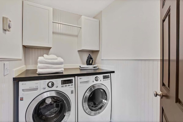 A laundry area with two front-loading washing machines, a drying rack, and a towel stack.