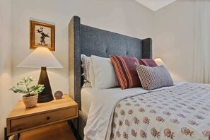 A neatly made bed with patterned bedding, a bedside lamp, a clock, and a framed picture on the nightstand.