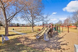 Un parque infantil con toboganes y estructuras para escalar, rodeado de árboles y un cielo despejado.