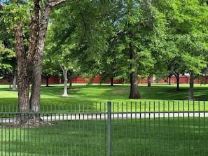 Un parque cercado con árboles grandes y un césped bien cuidado.