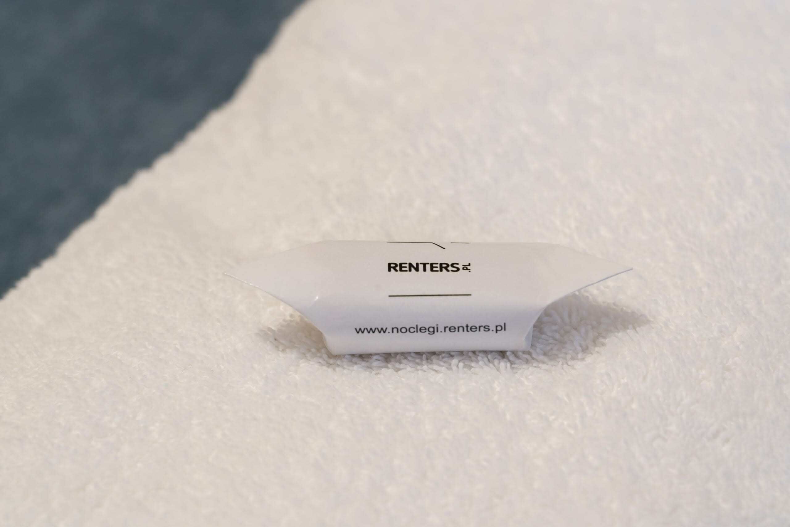 Un panneau blanc, de forme triangulaire, sur lequel figure le texte « RENTERS » et l’adresse d’un site web, « www.noclegi.renters.pl », le tout sur un fond blanc et duveteux.