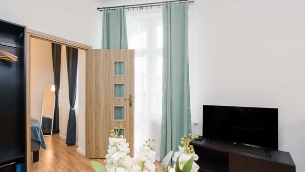 A modern living room with a wooden door, a flat-screen TV, and a large window with curtains.