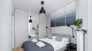 A modern bedroom with a bed, bedside tables, a radiator, and a large window with a view.