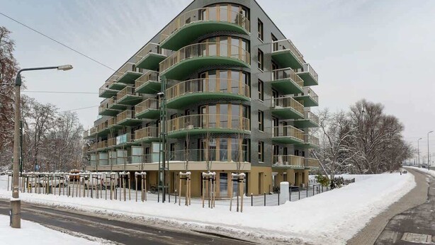 A multi-story building with balconies, a snow-covered ground, and a clear sky.