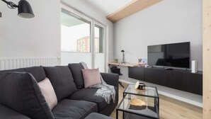 A modern living room with a dark sofa, a glass coffee table, a flat-screen TV, and a wooden ceiling.