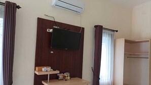 Habitación de hotel con televisor montado, repisa de madera con artículos de aseo, ventana con cortinas y armario empotrado.