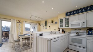 A kitchen with white cabinets, a microwave, and a stove. There is a sign that says "Beach House" on the wall. - Stunning Marsh and Bay Views from Beautiful 2 Bedroom Condo (Ocean City)
