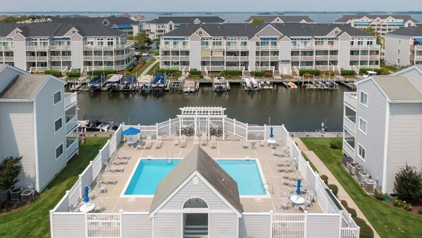 A waterfront hotel with a swimming pool, outdoor seating, and a dock with boats. - Stunning Marsh and Bay Views from Beautiful 2 Bedroom Condo (Ocean City)