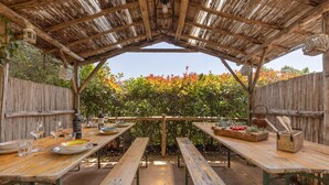 An outdoor dining area with wooden tables and benches, surrounded by a wooden fence and a thatched roof structure. - 3 bedroom gorgeous home in Orbicciano (Orbicciano)