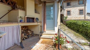 A rustic stone building with a wooden staircase leading to a door. A small garden with red flowers is visible outside. - 3 bedroom gorgeous home in Orbicciano (Orbicciano)