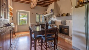 A rustic kitchen with exposed wooden beams, a dining table with chairs, a built-in oven, and a window with a view of greenery. - 3 bedroom gorgeous home in Orbicciano (Orbicciano)