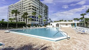Un hotel moderno con una piscina grande, diversi balconi e palme.