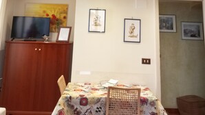 A room with a dining table, chairs, a TV, framed artwork, and a ceiling with a decorative pattern. - La Terrazza Apartment (Catania)