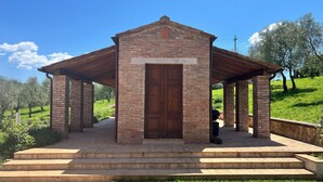 Un pavillon en briques doté d’une porte en bois et d’un escalier menant à l’entrée, entouré d’une pelouse et d’arbres.