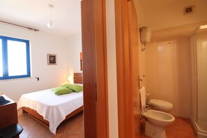 Une chambre à coucher comprenant un lit, une table de chevet, une fenêtre et une salle de bain avec des toilettes, un bidet et une douche.