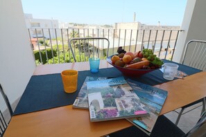 Une table avec un saladier de fruits, un magazine et un verre, sur un balcon d’où l’on peut admirer des bâtiments et la verdure.