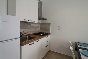 A compact kitchen with white cabinets, a stainless steel sink, a gas stove, and a built-in oven.
