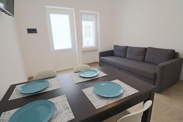 A dining table with four blue plates, a gray sofa, and two white chairs.