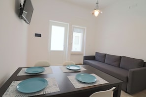 A dining table with four blue plates, a grey sofa, and a TV mounted on the wall.