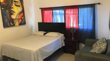 A bedroom with a bed, a nightstand, a lamp, a sofa, and a painting on the wall.