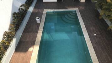 A rectangular swimming pool with a tiled deck surrounding it.