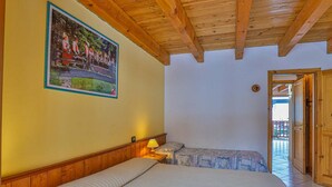 A room with two beds, wooden ceiling beams, a painting on the wall, and a door leading outside. - Apartment La Gran Becca - ID 3946 (Antey-Saint-Andre)
