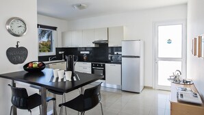 A modern kitchen with white cabinets, a black countertop, and a dining area with a black table and chairs. - Protaras holiday villa - rentprivatevillas 174 (Protaras)