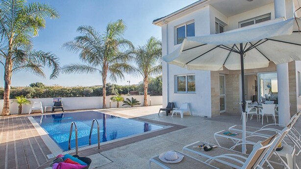 A modern two-story house with a swimming pool, outdoor seating, and palm trees. - Protaras holiday villa - rentprivatevillas 174 (Protaras)