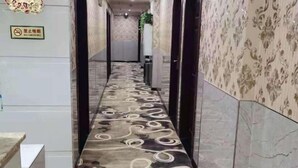 Un pasillo con alfombra estampada, un cartel de prohibido fumar y una planta al fondo.