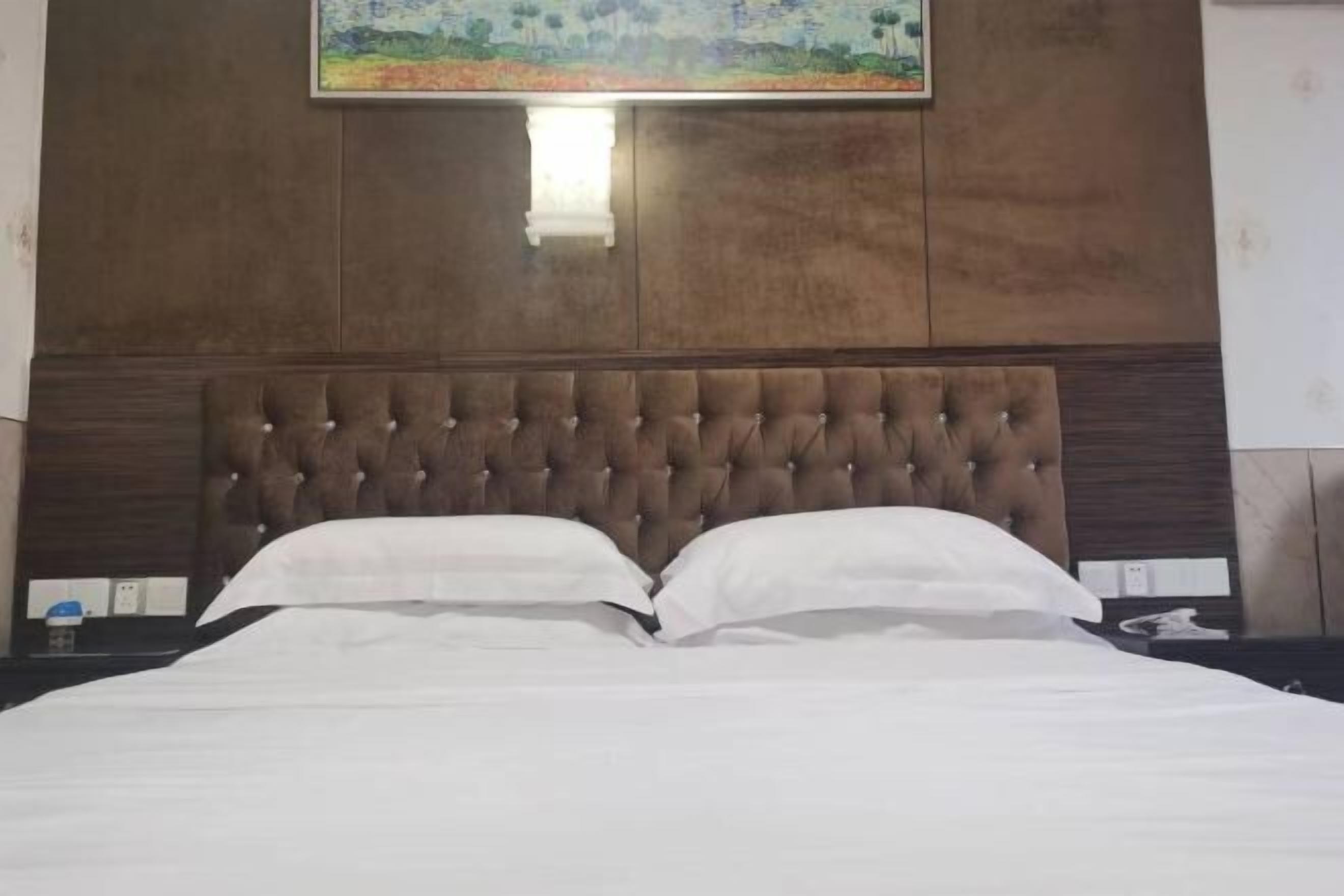 A neatly made bed with a tufted headboard, white bedding, and a painting above it.