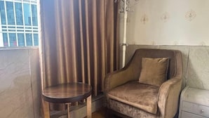 Una habitación de esquina con un sillón mullido, una mesita redonda y una mesita de noche.