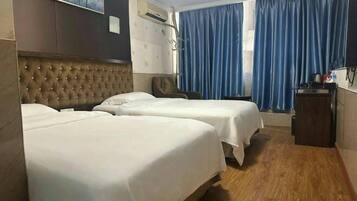 Una habitación de hotel con dos camas, un cabecero capitonado, aire acondicionado montado en la pared y una ventana con cortinas azules.