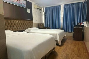 Una habitación de hotel con dos camas, un cabecero capitonado, aire acondicionado montado en la pared y una ventana con cortinas azules.