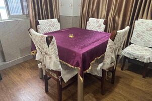 A dining area with a purple tablecloth, white upholstered chairs, and a window with curtains.