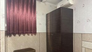 Una habitación con un armario de madera oscura, un pequeño banco marrón y una cortina roja.