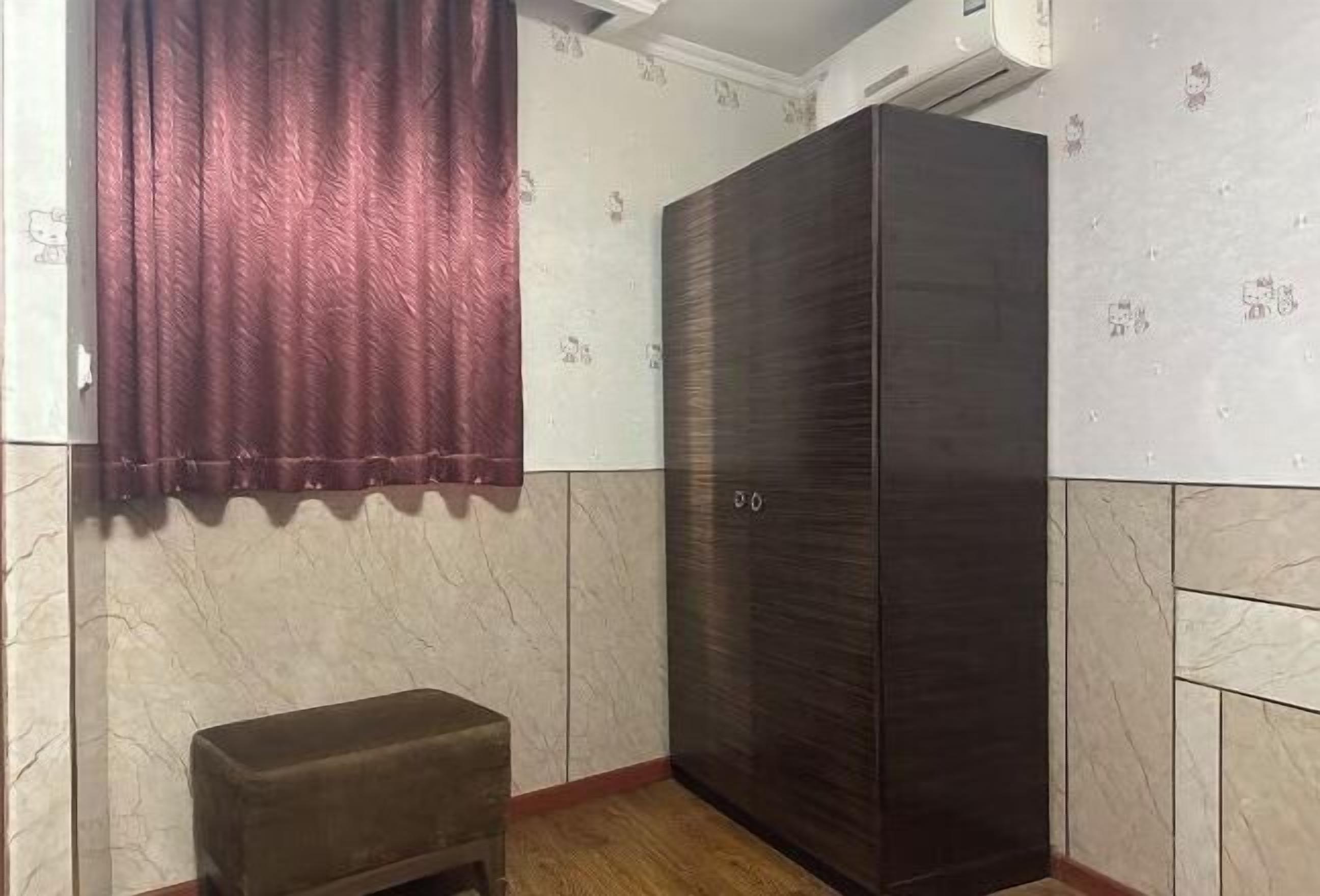 Une pièce avec une armoire en bois foncé, un petit banc marron et un papier peint à motifs.