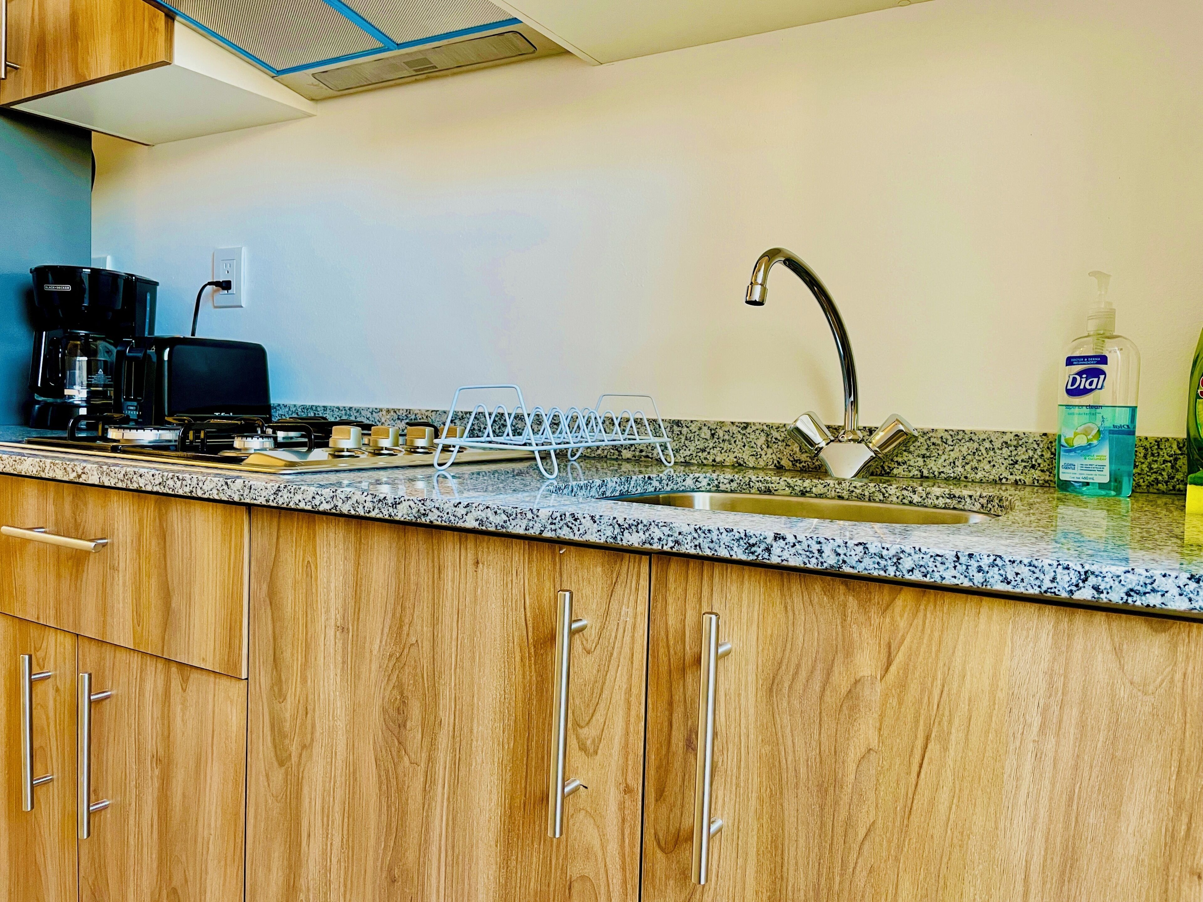 A kitchen with wooden cabinets, a stainless steel sink, a coffee maker, and a dish rack.