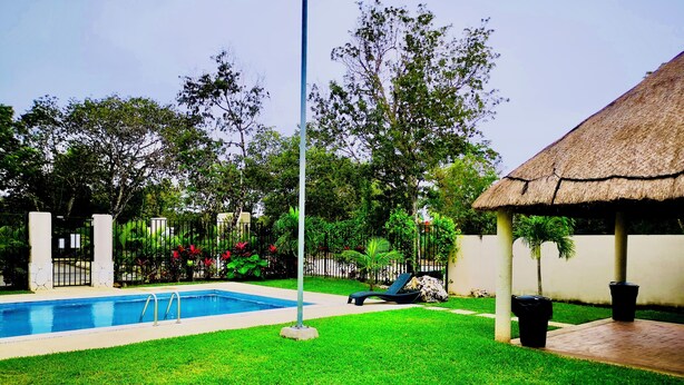 A swimming pool with a thatched-roof structure, surrounded by well-maintained grass and trees.