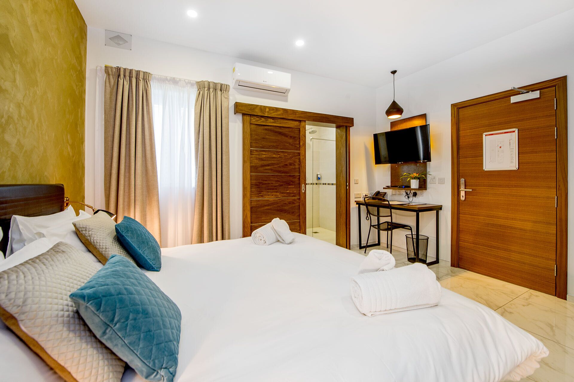 A hotel room with a large bed, a desk with a chair, a TV, and a shower area.
