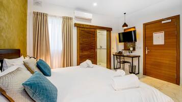 A hotel room with a large bed, a desk with a chair, a TV, and a shower area.