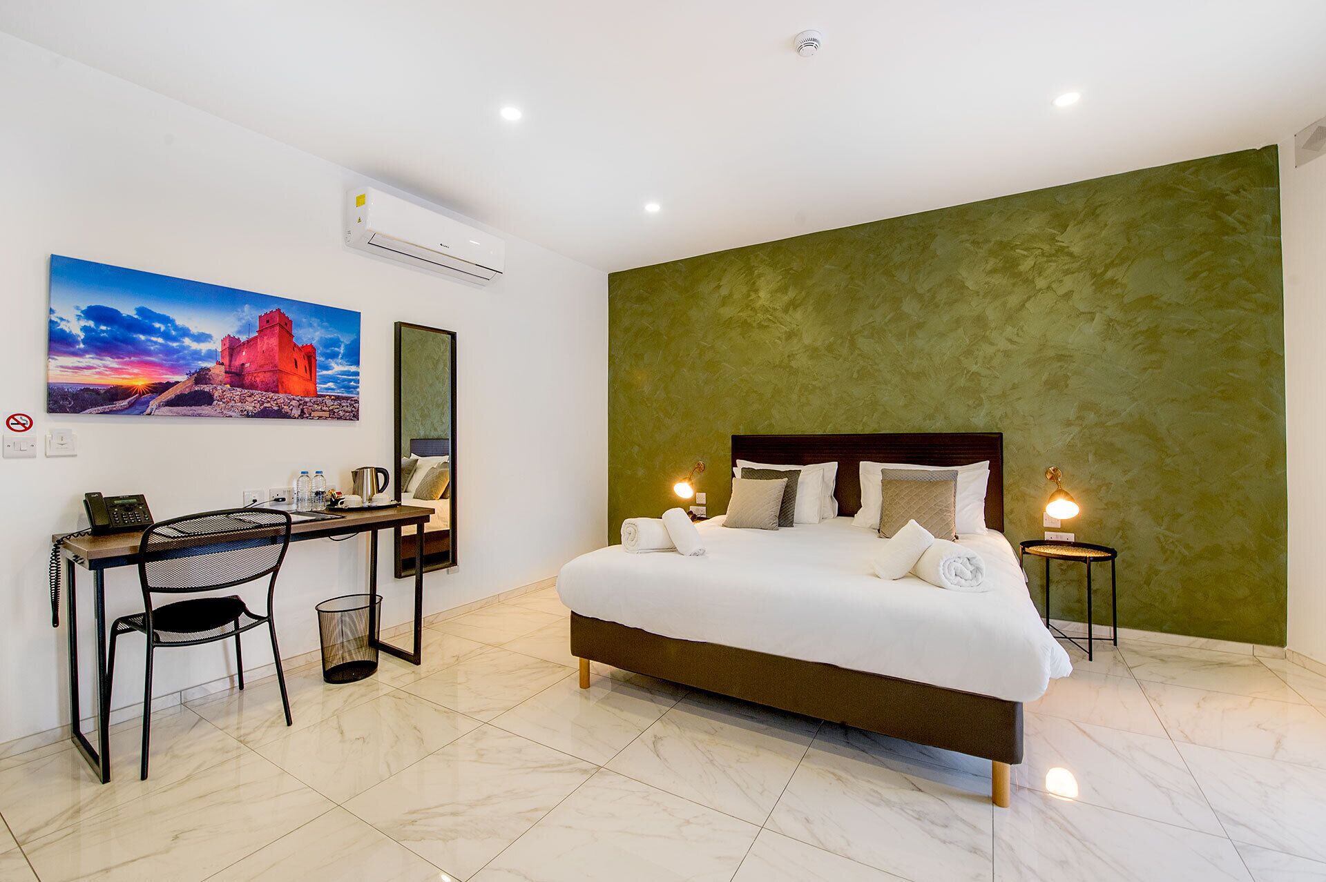 Een hotelkamer met een groot bed, een bureau met stoel, een telefoon en een wandairconditioner.