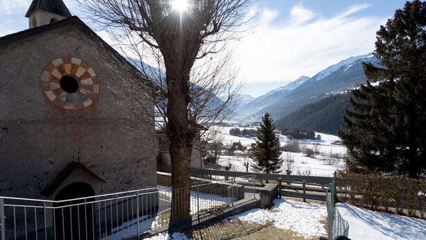 Une église dotée d’une fenêtre circulaire et offrant une vue sur des montagnes enneigées.