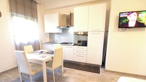 A modern kitchen with white cabinets, a gas stove, and a built-in oven. There is a dining table with chairs and a TV mounted on the wall. - Holiday House 'casa Vacanze Alba A Otranto' With Balcony and air Conditioning (Otranto)